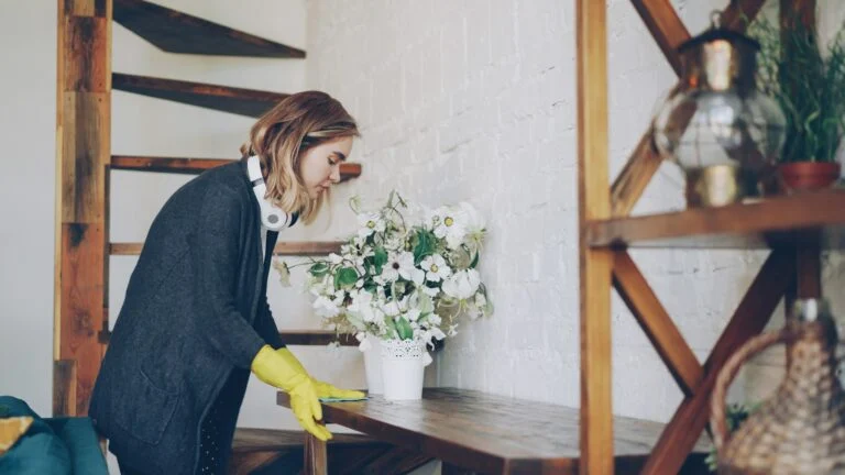 Cleaner in yellow gloves dusting a shelf